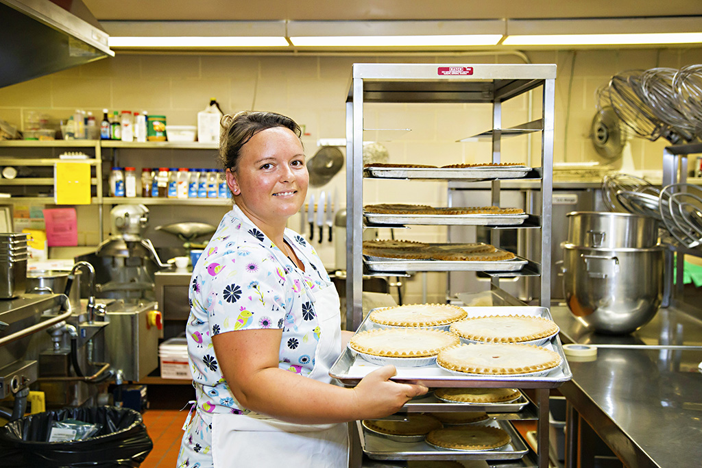 Kitchen staff member holidng a tray of fresh baked pies