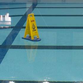A picture of a Wet Floor sign floating on a fullterboard along the surface of a pool.