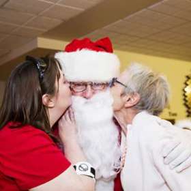 A resident and her daughter kissing Santa on the cheek